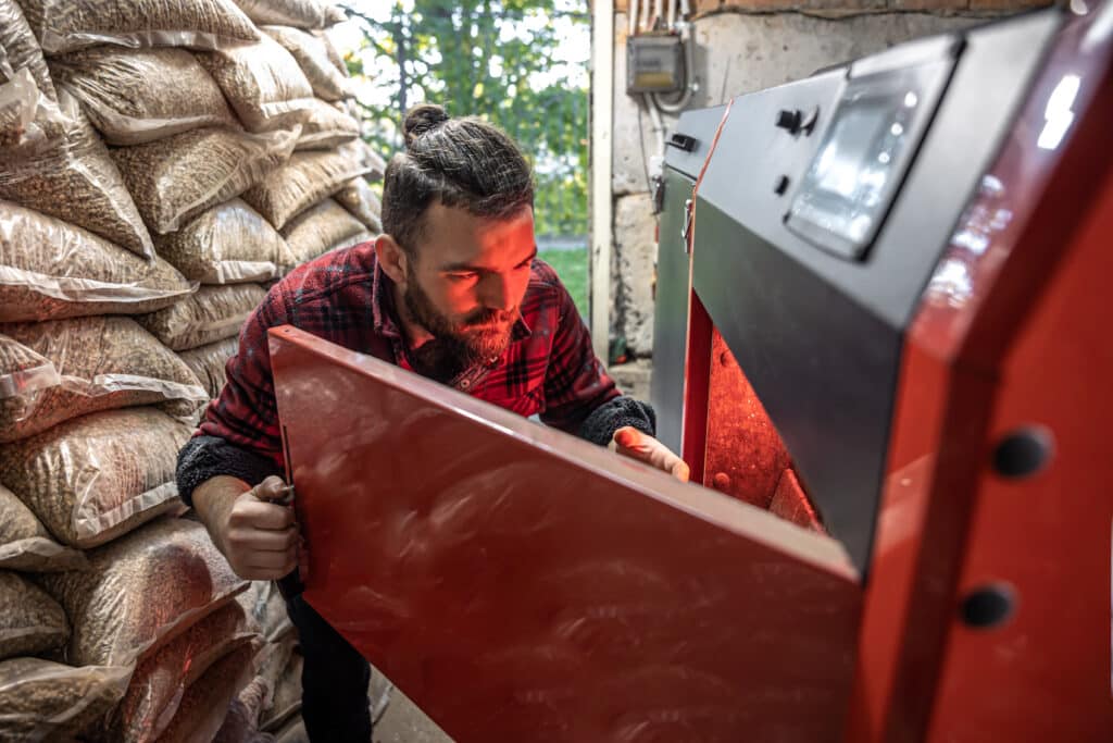 Young man looking into a solid fuel boiler burning biofuel